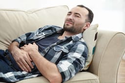 Hombre guapo sufriendo de dolor de estómago mientras está acostado en el sofá en casa. Tratamiento complementario de acupuntura para dolor abdominal crónico