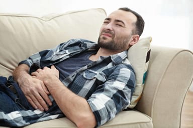 Hombre guapo sufriendo de dolor de estómago mientras está acostado en el sofá en casa. Tratamiento complementario de acupuntura para dolor abdominal crónico