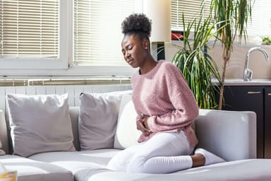 Mujer afroamericana con expresión dolorosa tomándose de la mano contra el vientre que sufre dolor menstrual, eficacia del tratamiento homeopático en el dolor premenstrual